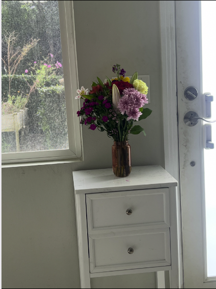 Curated flower arrangement on a white side table by a sunlit window — Nora's eye for detail