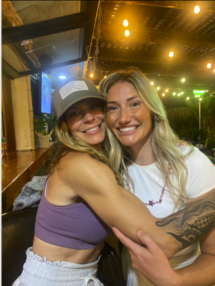 Nora with a friend at an Encinitas patio bar — golden lights, real warmth
