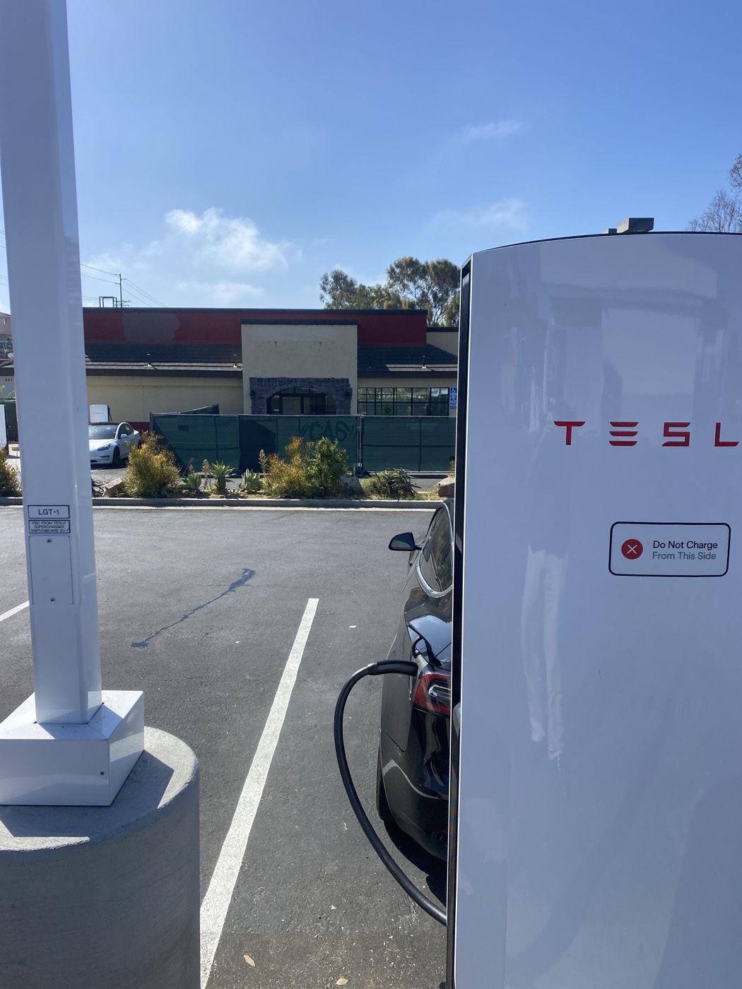 New Tesla V4 Supercharger posts on Birmingham Dr in Cardiff, with the former Mexico Viejo building fenced for construction behind them, Oct 1 2026