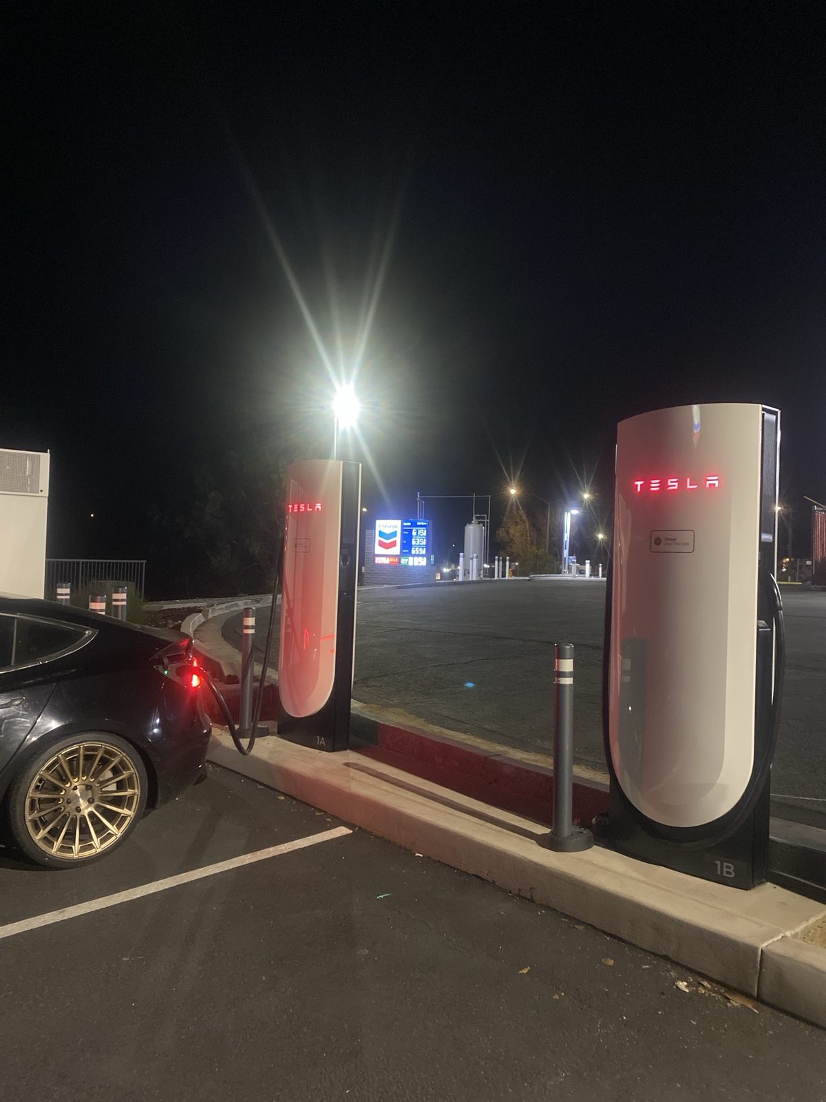PJ's car charging at the Cardiff Tesla Supercharger before sunrise, the Chevron sign next door showing Regular 6.19
