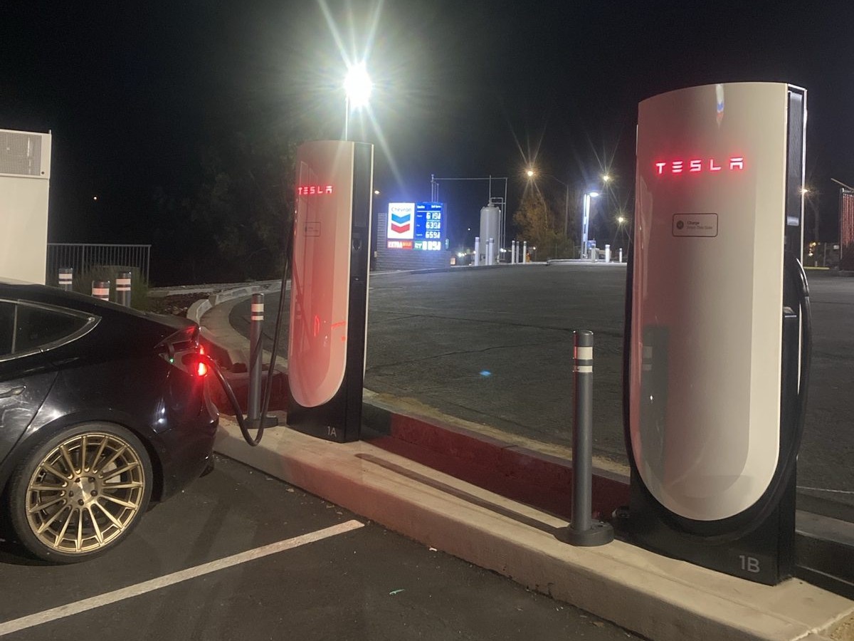 PJ's black Tesla charging at stall 1A of the Cardiff Supercharger before sunrise, the red Tesla logos lit on two posts