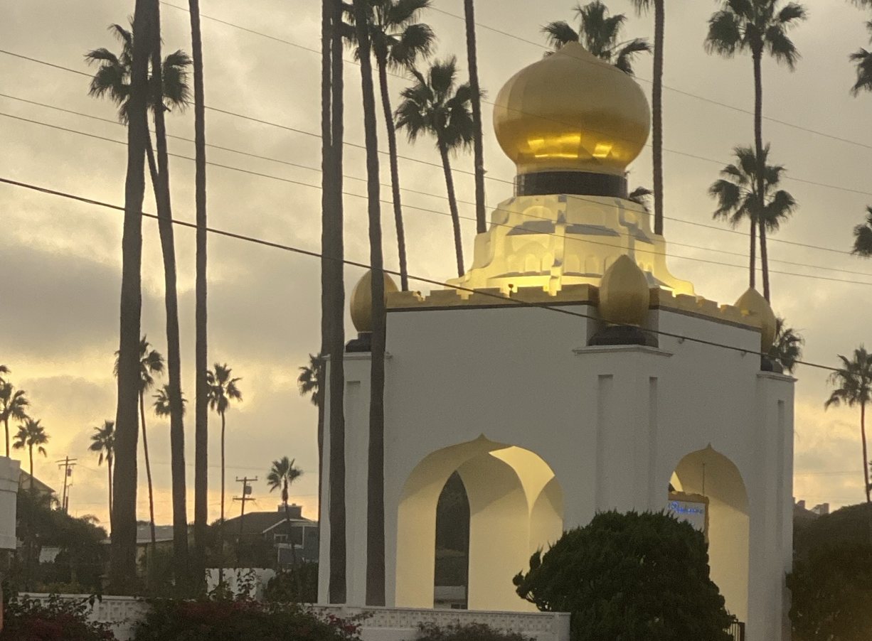 The Self-Realization Fellowship golden lotus towers glowing under tall palms at dusk on Highway 101 by Swami's in Encinitas